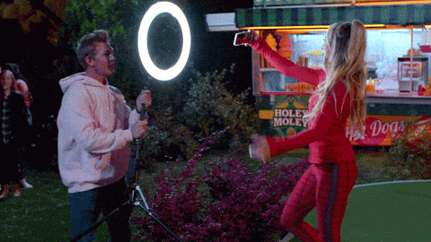 A man holding a ring light for a woman as she takes a video of herself