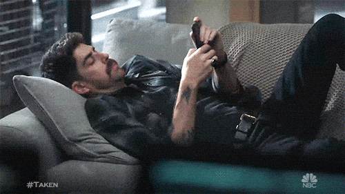 A man laying on the couch scrolling on his phone.