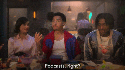 A man on a couch at a party next to two others saying, 'Podcasts, right?'