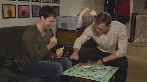 Daniel Craig and Taran Killam playing Monopoly. Craig gets frustrated and flips the board upside down.