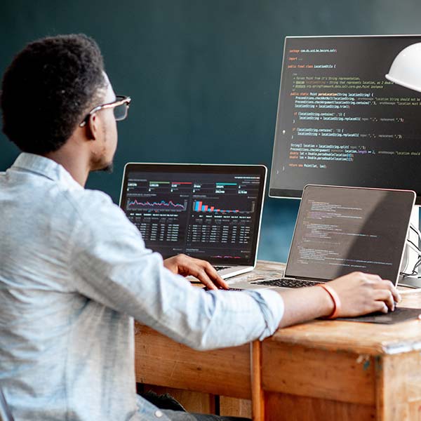 Man coding in front of several computer screens