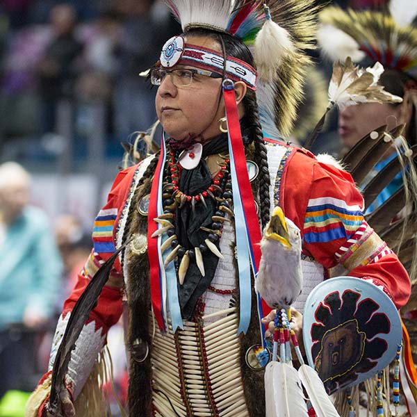 A man in traditional Native clothing looking to the crowd at a conference